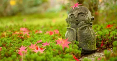 Red Maple leaf on head of little Japanese Buddhist monk doll rock in Japanese Garden